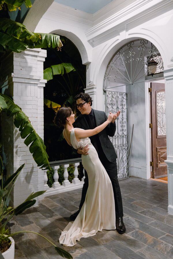 Bride and groom dance outside on porch near giant palm tree leaves