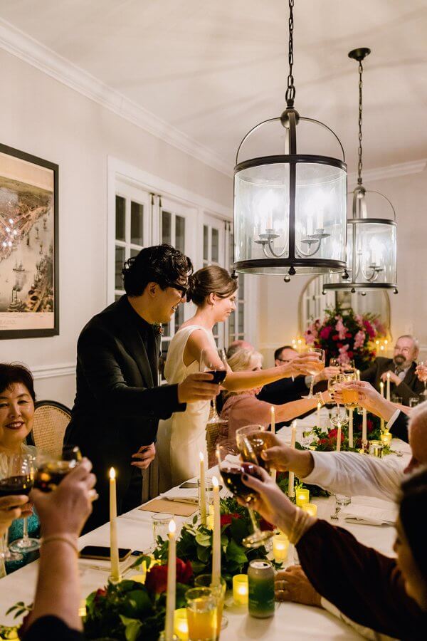 Group cheersing at a small dinner wedding party while the bride and groom stand