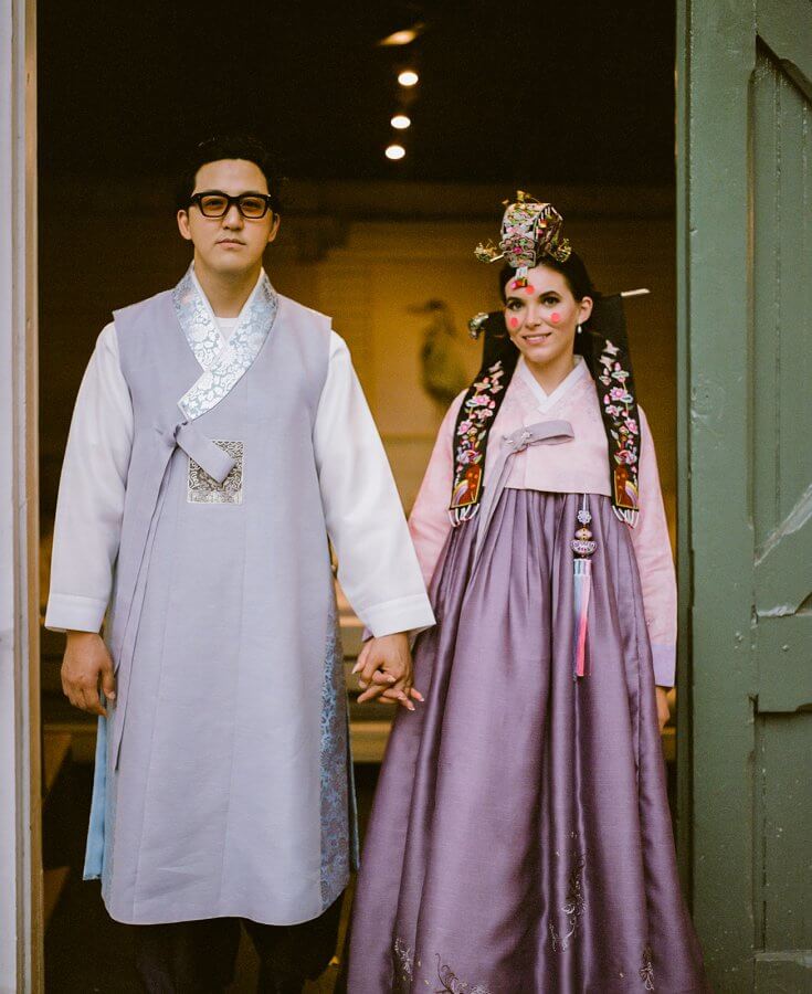 Groom and bride stand in a doorway in traditional Korean hanbok outfits