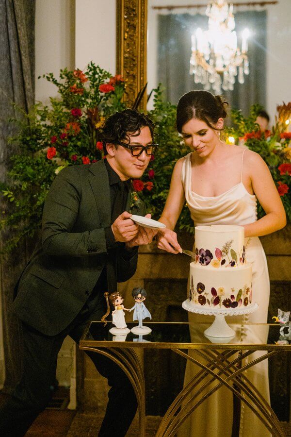 Groom and bride cut a two-tiered wedding cake with flowers on the sides