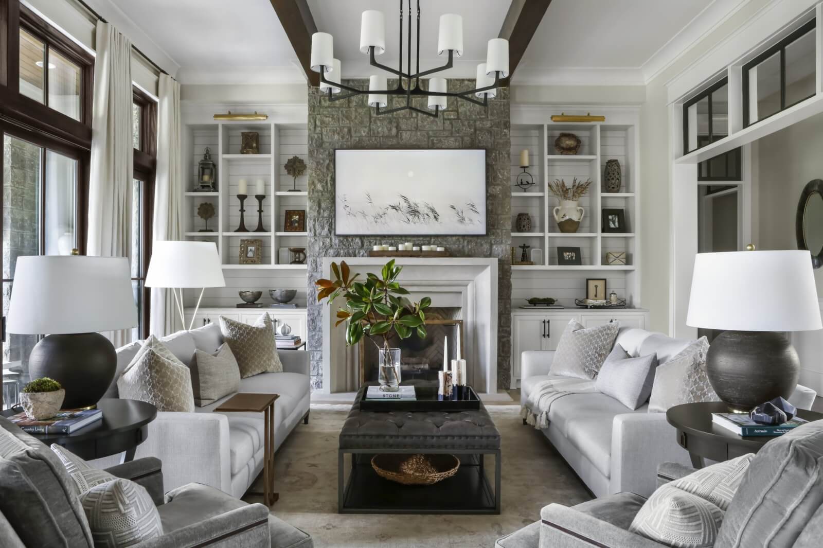 Living room with black outlined windows, silver couches, and a stone fireplace.