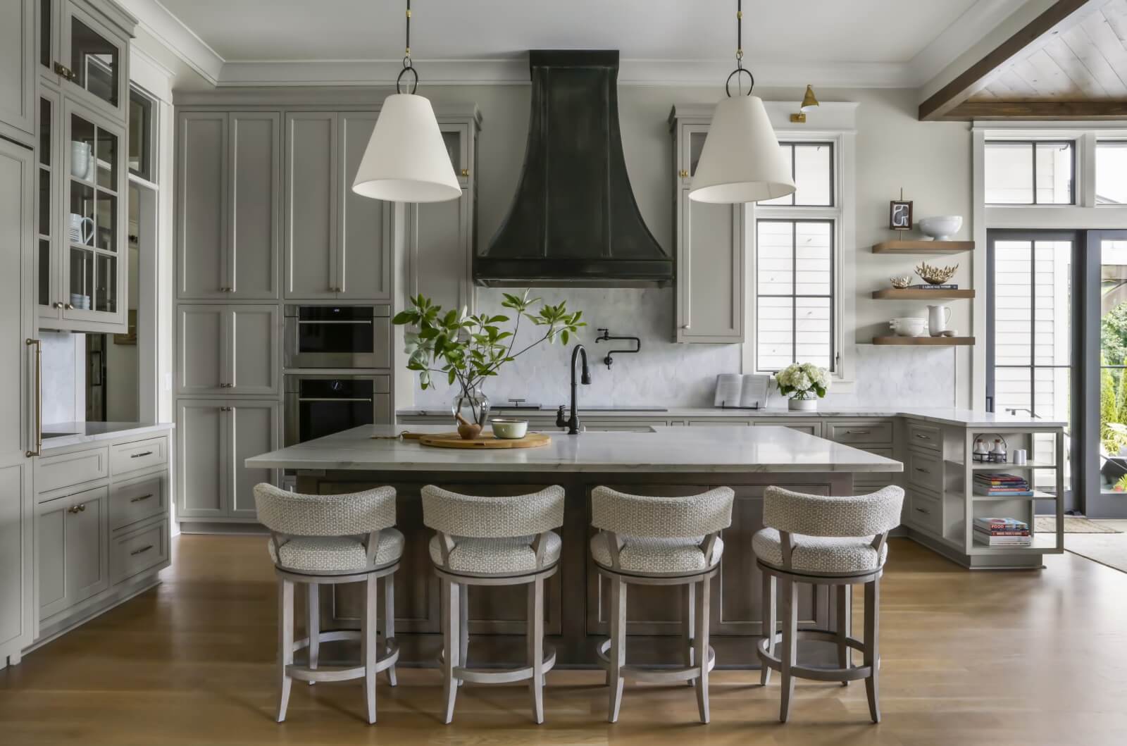 Kitchen with light gray cabinetry and a kitchen island with four stools. 