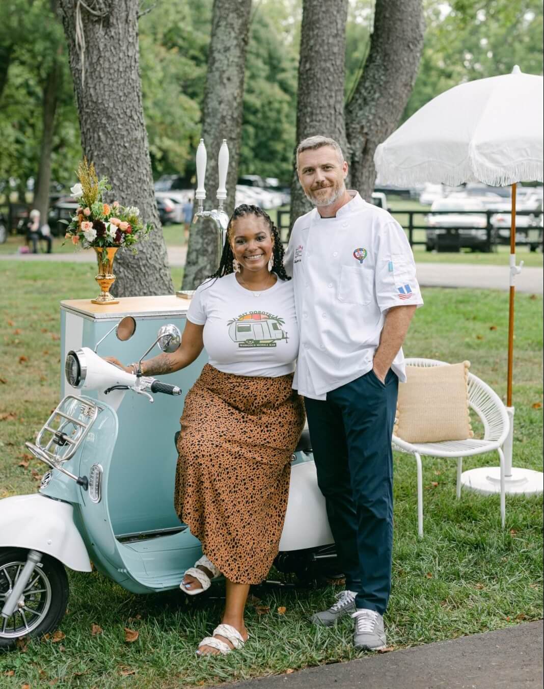 husband and wife pose in front of pale blue mobile bar