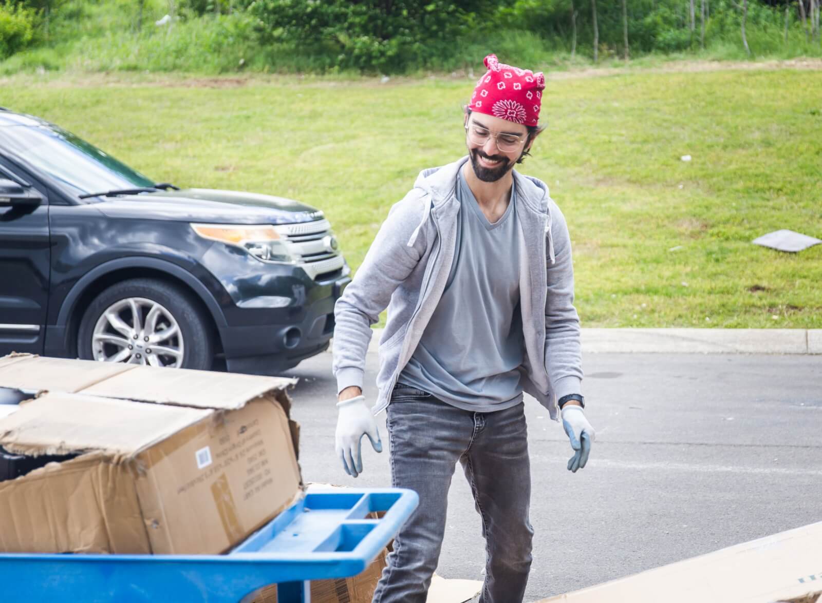 A-Stock employee smiling and looking at a cart of cardboard boxes.