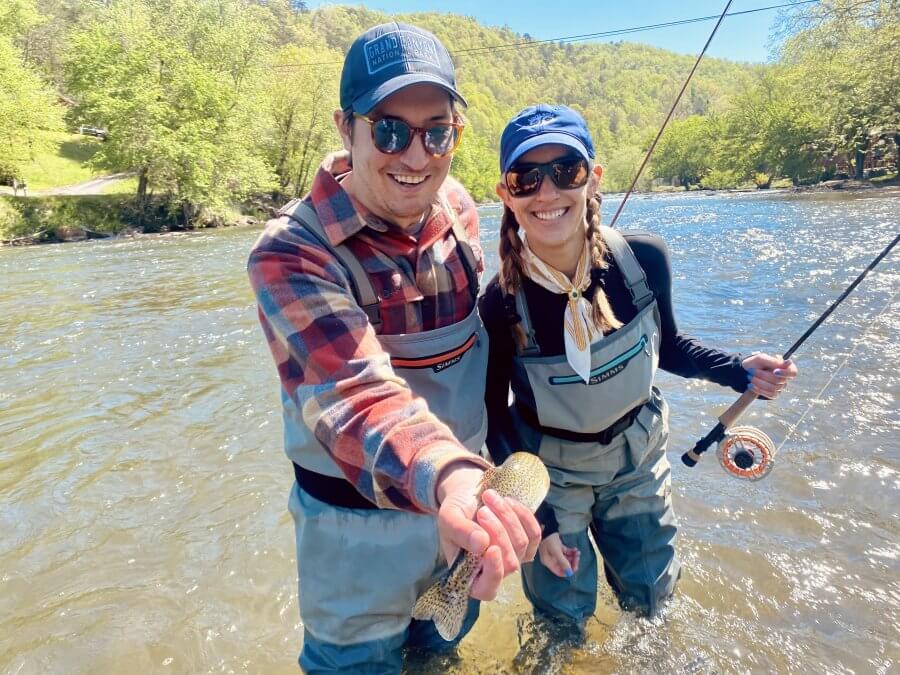 A man and woman stand in the Tuckasegee River with a trout fly fishing